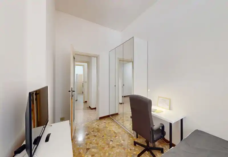 Dormitorio pequeño y ordenado con cama individual, escritorio y armario con espejo. La habitación es luminosa y de decoración mínima, ideal para una persona o estudiante.