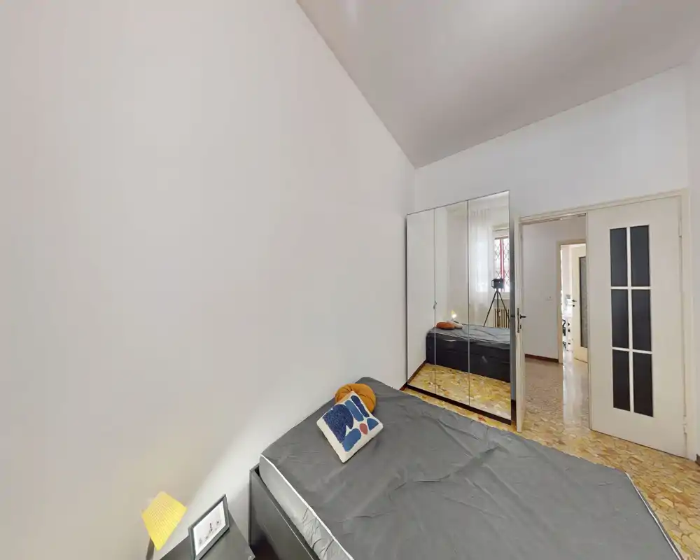 Dormitorio ordenado con cama doble, cojín decorativo y lámpara de mesita; un gran armario con espejo aumenta la luminosidad y la sensación de amplitud.