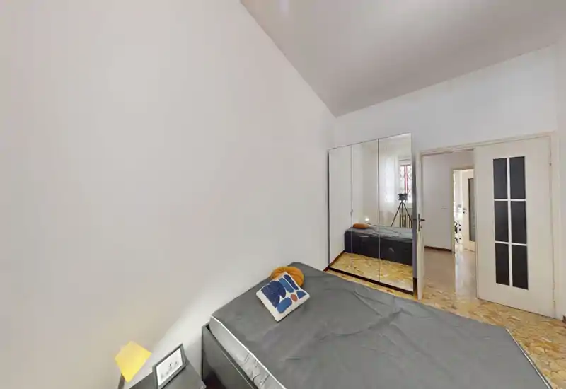 Dormitorio ordenado con cama doble, cojín decorativo y lámpara de mesita; un gran armario con espejo aumenta la luminosidad y la sensación de amplitud.