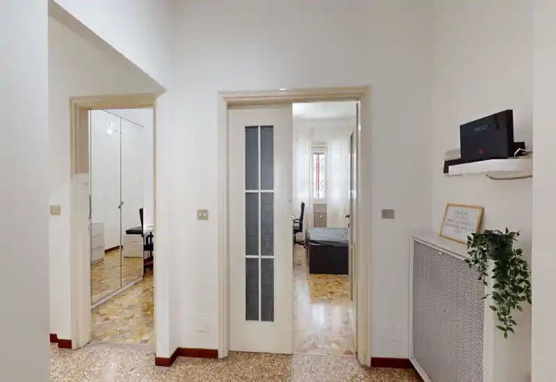 Dormitorio luminoso y ordenado visible a través de una puerta abierta: cama doble y luz natural de la ventana crean un espacio acogedor para dormir.