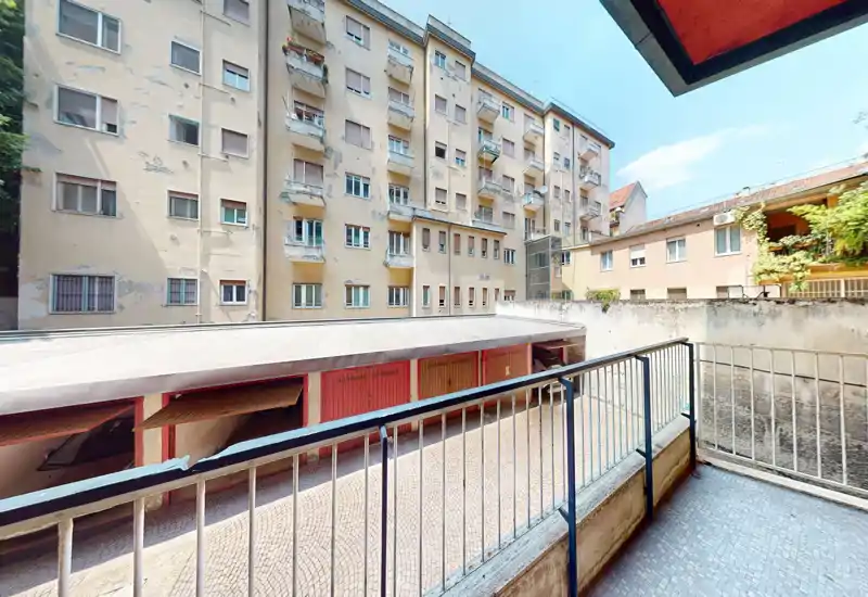 Pequeño balcón soleado con vistas a un patio interior y garajes; suelo cerámico y barandilla metálica que ofrecen un espacio exterior práctico.