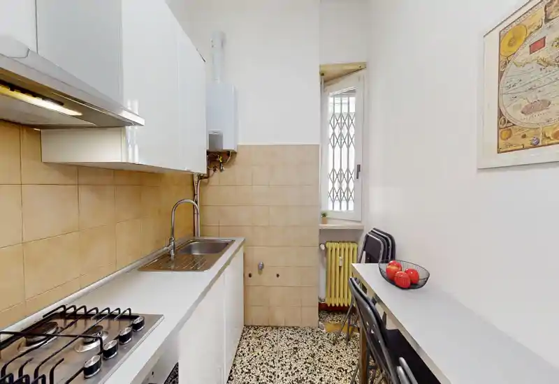 Cocina compacta y luminosa con placa de gas, fregadero sencillo, salpicadero de azulejos y una barra estrecha — práctica para un piso pequeño.