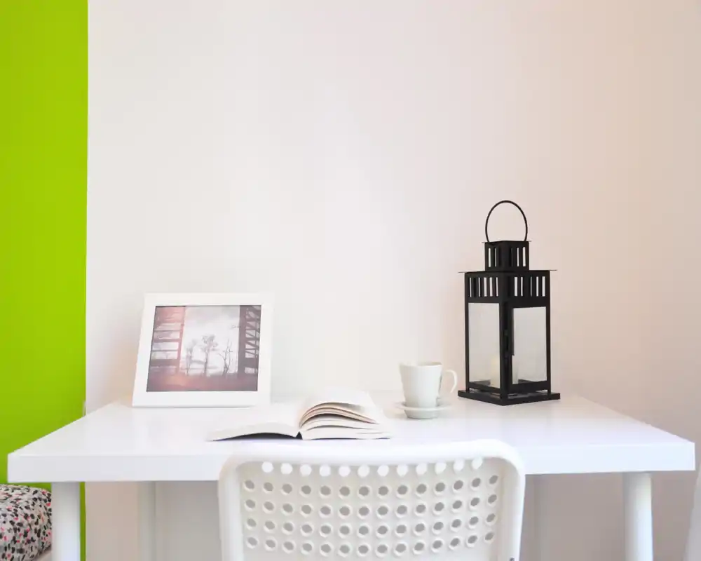 Coin salon lumineux et minimaliste avec bureau blanc, lanterne décorative, photo encadrée, livre ouvert et tasse — un espace calme et cosy pour lire ou travailler.