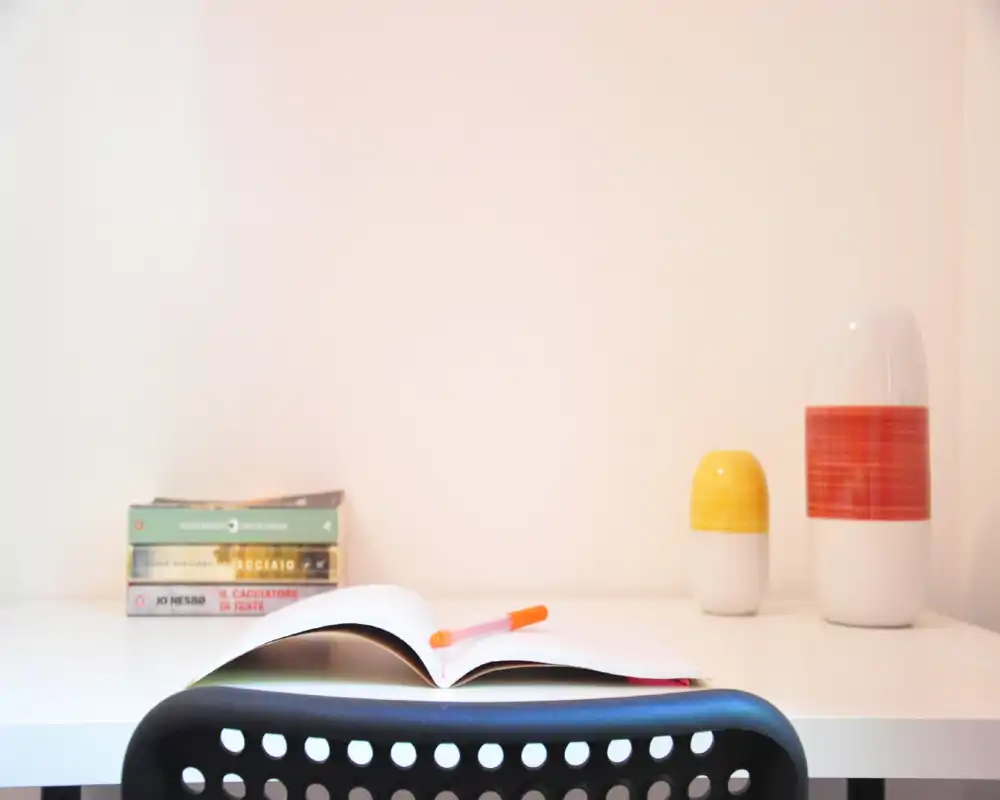 Angolo studio luminoso e minimal con scrivania bianca, quaderno aperto e penna, libri e vasi decorativi — perfetto per mostrare uno spazio per lavorare da casa.