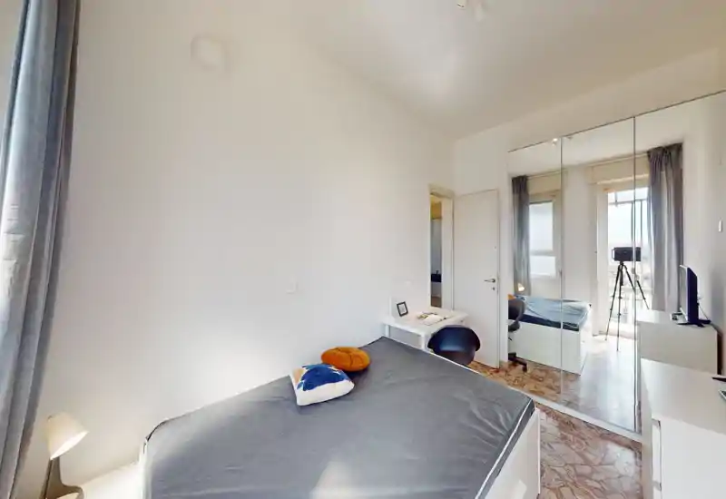 Chambre lumineuse et bien décorée avec lit double, lampe de chevet et placard miroir reflétant la fenêtre — idéale pour des annonces valorisant l'espace et la lumière.