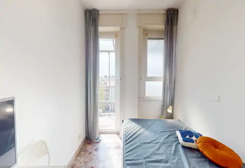 Chambre simple lumineuse avec lit bien fait, grandes fenêtres et rideaux clairs apportant beaucoup de lumière naturelle—compacte et minimaliste, idéale pour une personne.