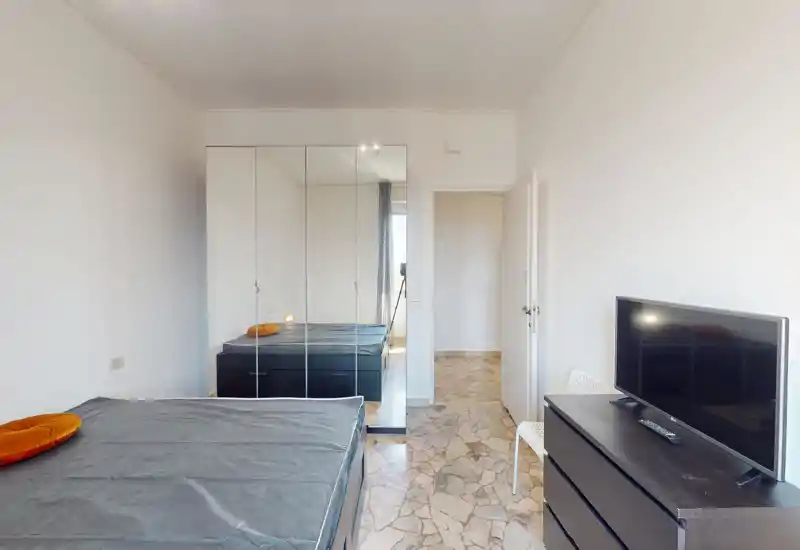 Chambre lumineuse avec lit double, placard à portes miroir et commode avec télévision. Espace simplement meublé, murs neutres et lumière naturelle provenant de la fenêtre.