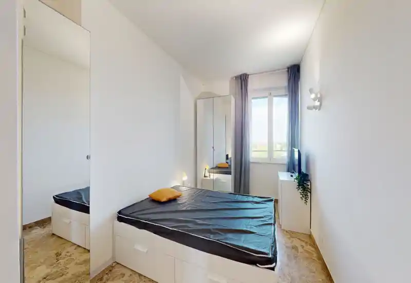 Bright, modern bedroom with a neatly made double bed, full-length mirror, wardrobe and a window that fills the room with natural light.