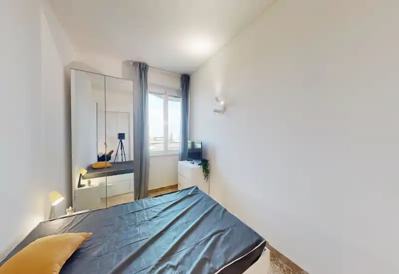 Minimal, bright bedroom with a double bed in the foreground, a mirrored wardrobe, bedside lamps and a window providing natural light. The room is simply styled and feels airy and inviting.