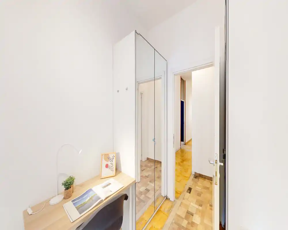Compact, bright entrance/hallway with a mirrored wardrobe and a small wooden desk — clean white walls and parquet flooring create a neat, welcoming arrival space.