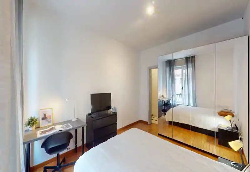 Bright, neatly staged bedroom with a double bed, mirrored wardrobe and a small desk by the window — ideal for rental listings highlighting space and natural light.