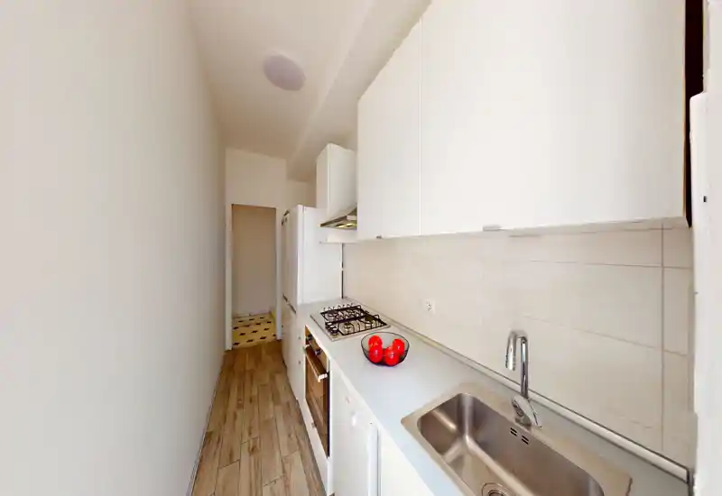 Cuisine étroite et moderne avec meubles blancs, plaque à gaz, évier inox et sol effet bois ; lumineuse et bien organisée pour un usage efficace.