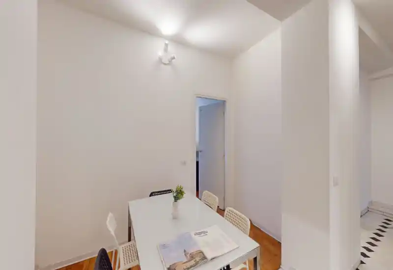 Coin repas minimaliste avec table blanche, quatre chaises et un petit vase ; murs lumineux et style épuré, idéal pour un appartement compact.