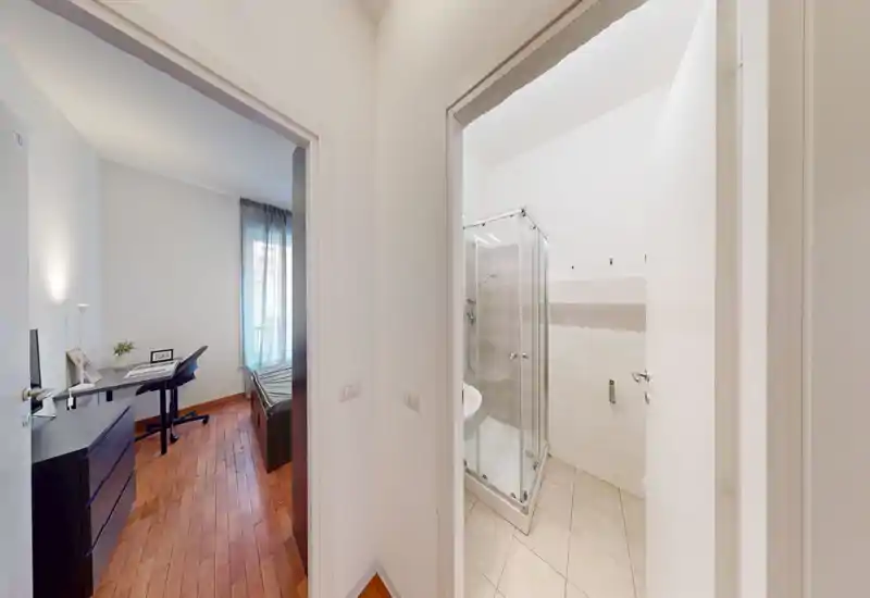 Chambre lumineuse et sobre avec lit simple, bureau et commode, parquet et lumière naturelle provenant d'une fenêtre.
