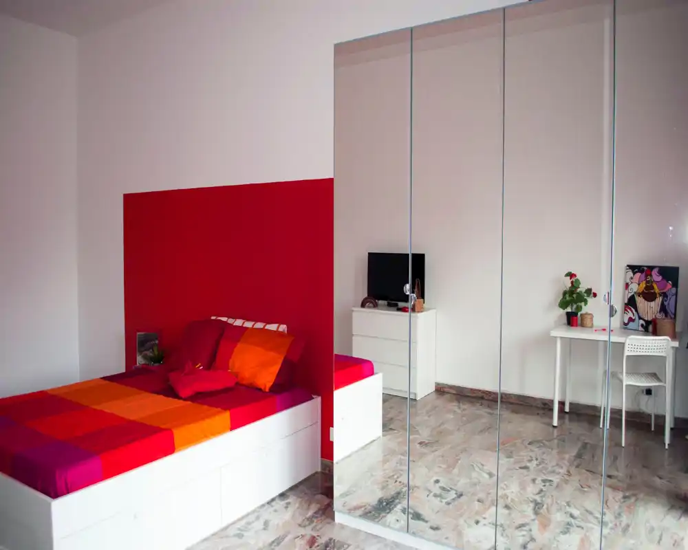 Bright, modern bedroom with a colorful double bed, mirrored wardrobe and a small desk — ideal for rental listings highlighting storage and style.