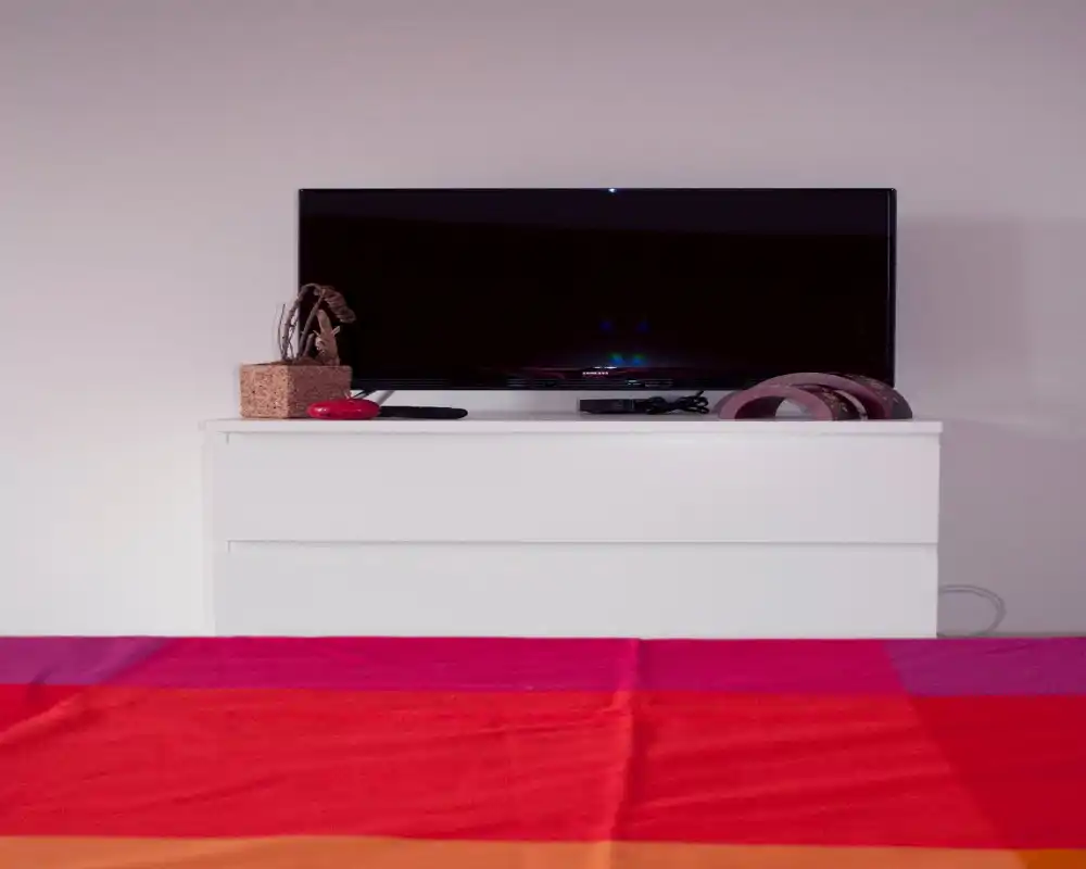 Minimal bedroom view focused on a dresser with a TV and a colorful bedspread in the foreground, offering a clean, modern feel.