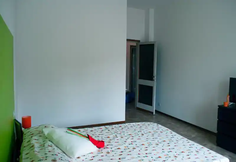 Chambre lumineuse et sobre avec un lit double aux draps imprimés, une lampe de chevet et des murs blancs apportant une ambiance fraîche et minimaliste.