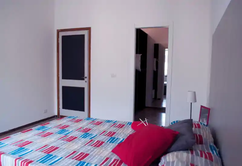 Chambre lumineuse et soignée avec un lit double à motifs au premier plan, coussins colorés et une lampe de chevet pour une ambiance accueillante.