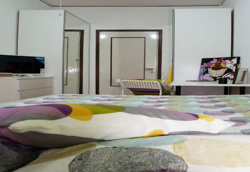 Dormitorio ordenado y luminoso centrado en una colcha con estampado, con escritorio y armario al fondo; decoración colorida adecuada para un anuncio.