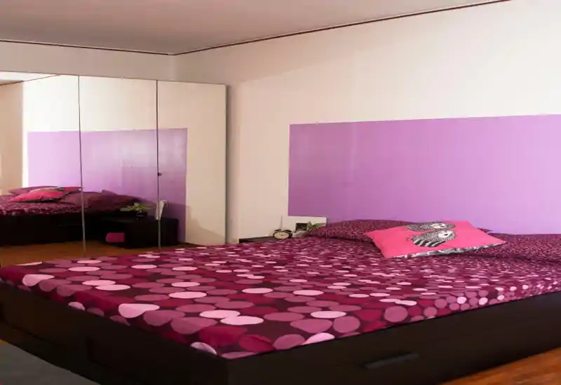 Dormitorio luminoso y con estilo con una cama grande cubierta con ropa de cama morada de lunares, almohadas a juego y un armario con espejos que amplía el espacio.