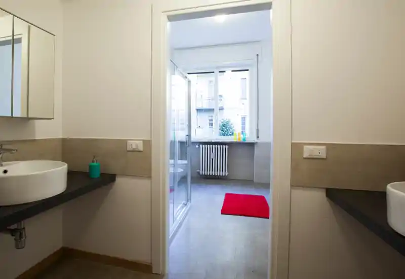 Bagno moderno e luminoso con due piani lavabo, una cabina doccia e una grande finestra che dona luce naturale.