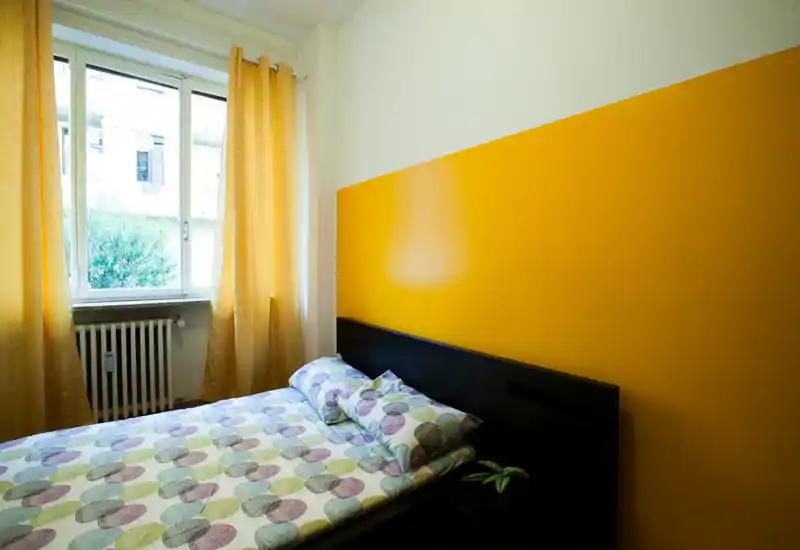 Camera da letto luminosa e accogliente con letto matrimoniale, parete d'accento gialla e ampia finestra che offre luce naturale.