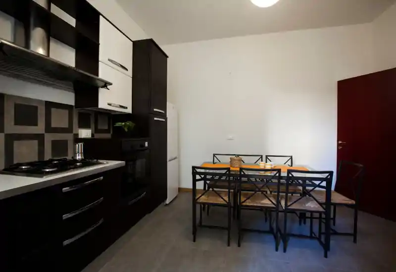 Cocina bien equipada con una mesa comedor compacta para seis. Muebles oscuros, salpicadero de azulejos y electrodomésticos integrados crean un espacio moderno y funcional.