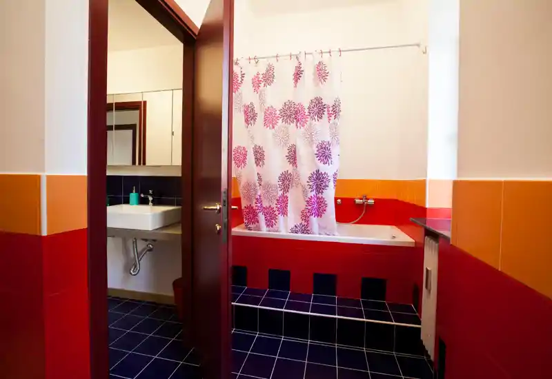 Bright, colorful bathroom with a bathtub behind a floral shower curtain, sink with mirror and dark tiled floor — a fresh, well-lit space.