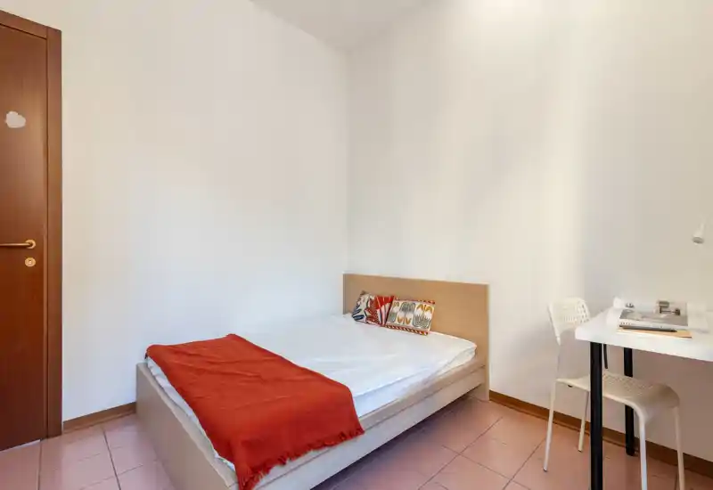 Chambre simple et lumineuse, lit en bois avec coussins colorés et plaid rouge, avec un petit bureau et une chaise — parfaite pour étudiant ou locataire seul.