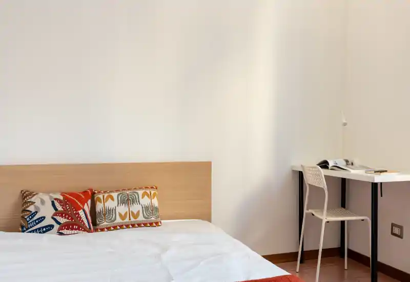 Dormitorio minimalista y luminoso con cabecero de madera, cojines decorativos y un pequeño escritorio junto a la pared — estilo limpio y sencillo, ideal para un huésped.