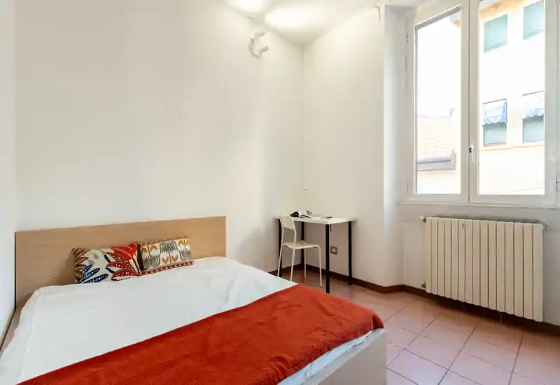 Chambre lumineuse et minimaliste avec lit double, coussins décoratifs et petit bureau près de la fenêtre — idéale pour une personne seule ou des séjours courts.