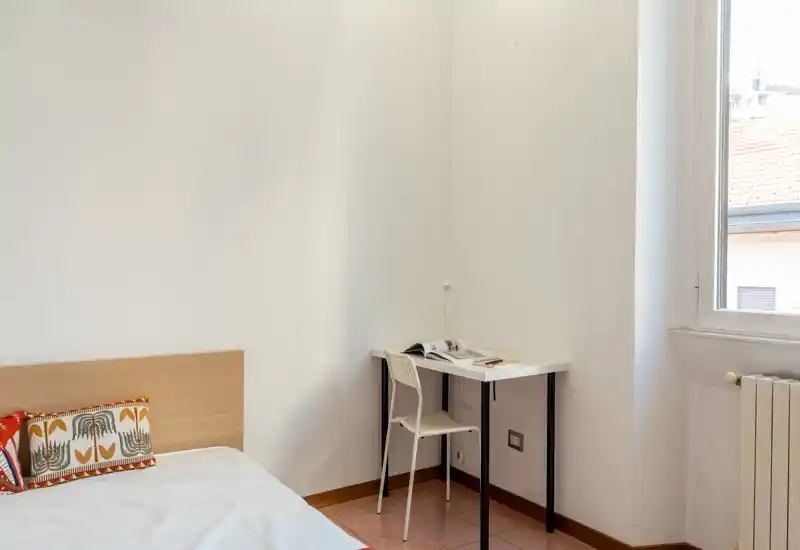 Dormitorio luminoso y minimalista con cabecero de madera, ropa de cama blanca y un pequeño escritorio junto a la ventana — ideal para una persona o estudiante.
