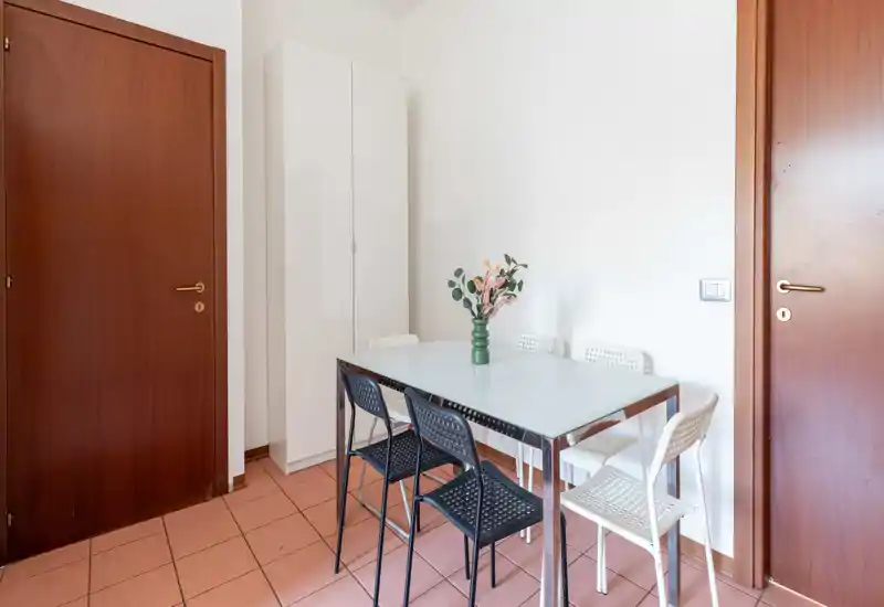 Compact dining area with a modern glass-top table and mixed black and white chairs, styled with a simple vase of flowers; bright, clean space suitable for casual meals.