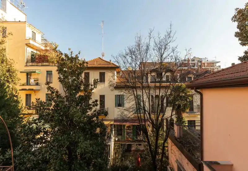 Vista desde un balcón con edificios residenciales y copas de árboles, con luz cálida y cielo despejado.