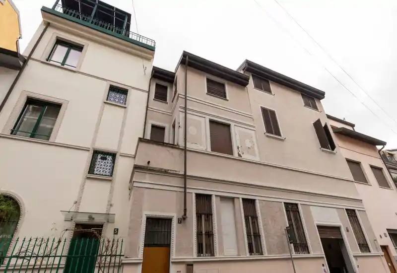 Vista exterior de la fachada de un edificio residencial de varios pisos con persianas y accesos a nivel de calle; iluminación suave y nublada que destaca los detalles arquitectónicos.