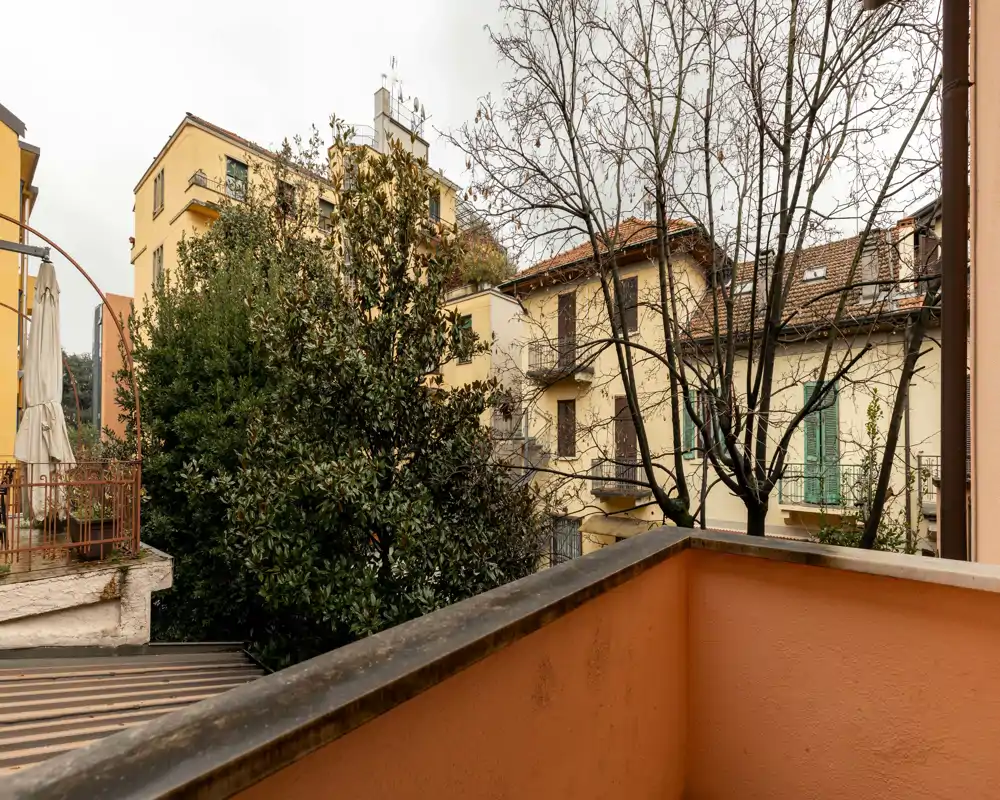 Small private balcony with urban view overlooking neighboring buildings and trees; suitable for a chair and plants, ideal for morning coffee.