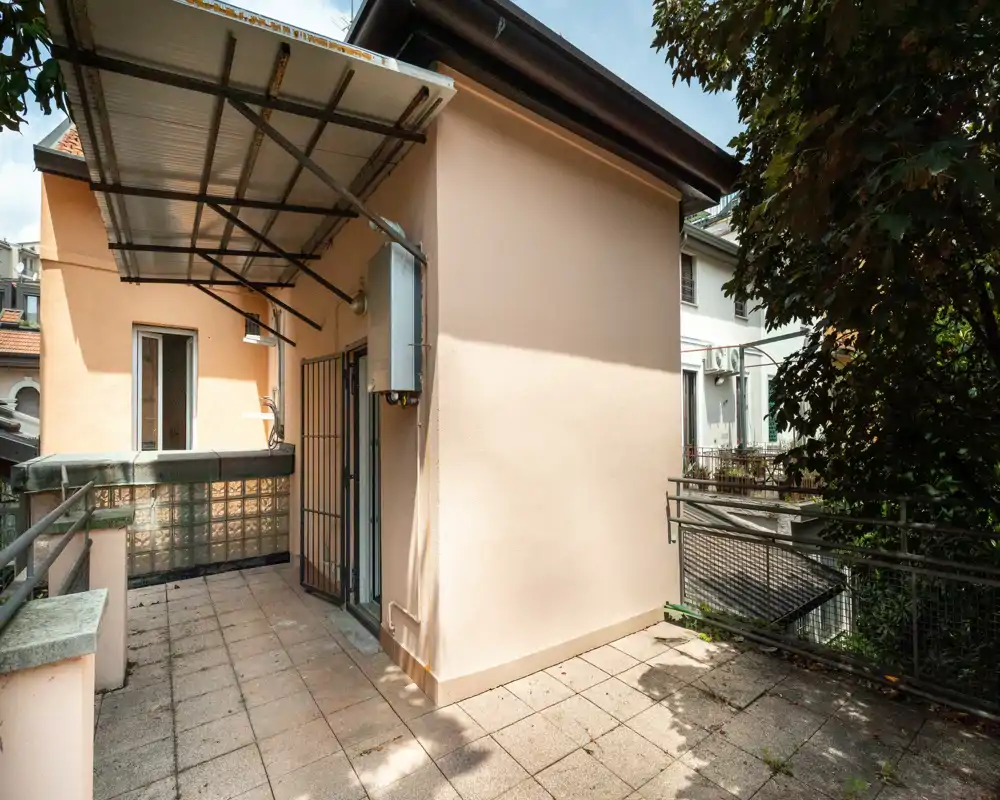 Sunny private terrace with tiled floor, metal railing and partial canopy — suitable for seating or plants and offering privacy with surrounding greenery.