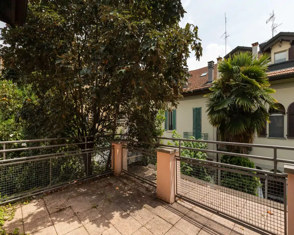 Sunny private terrace with tiled floor, metal railing and mature trees providing shade and privacy — ideal for outdoor relaxation.