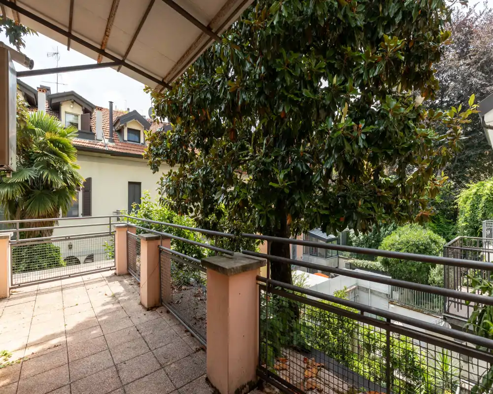 Sunny covered terrace with metal railings, tiled floor and lush greenery — ideal for morning coffee or relaxing outdoors.