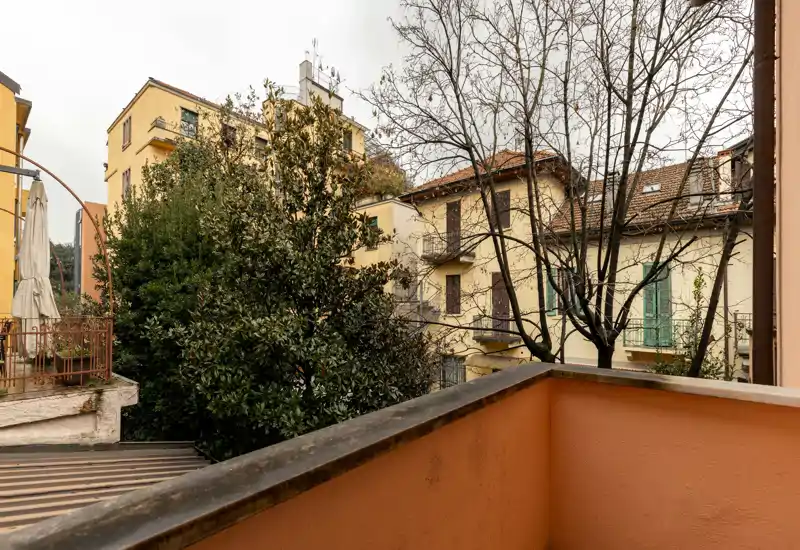 Sunny-feel urban balcony overlooking neighboring buildings and mature trees — a small private outdoor space ideal for a morning coffee.