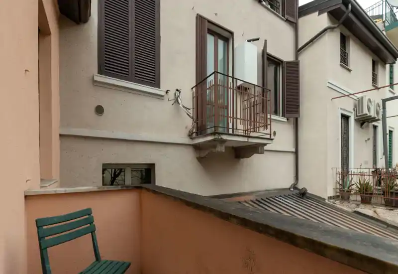 Small private balcony overlooking neighboring building façades, with a simple green folding chair and terracotta-colored walls—ideal for a morning coffee.