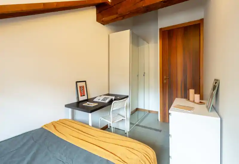 Bright, cozy bedroom with visible bed, wooden ceiling beams and a small desk area — ideal for a single occupant or short stays.