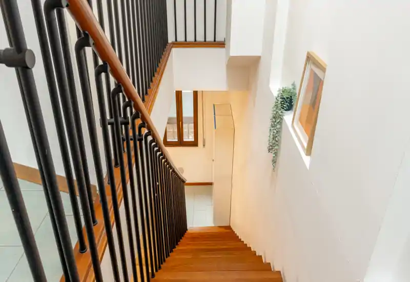 Bright, modern staircase and hallway entrance with wooden steps, black metal balustrade and a small landing illuminated by natural light.