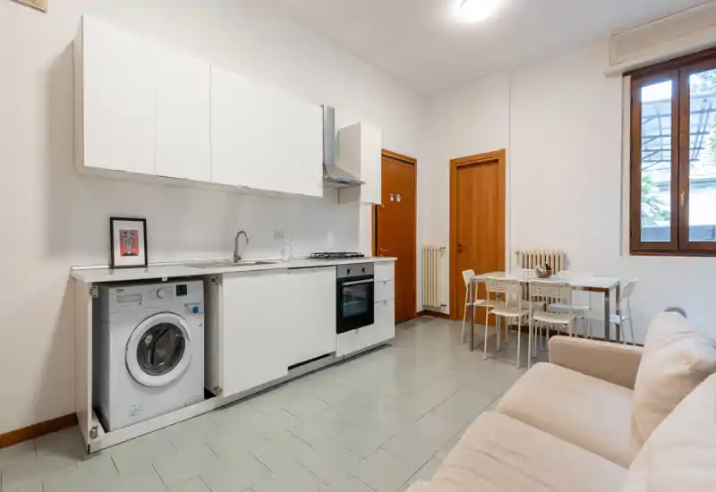 Bright and tidy open living area with a compact kitchenette, dining table for four and a light-coloured sofa — ideal for a small apartment or studio.