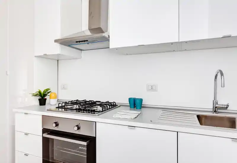 Bright modern kitchen with white cabinets, a gas hob, built-in oven and a stainless sink. Simple, well-styled surfaces with small decorative accents and ample counter space.