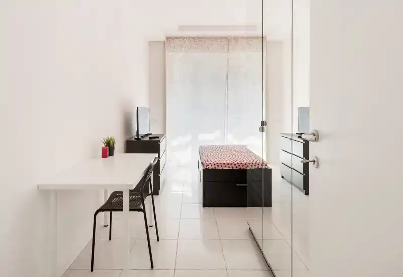 Dormitorio individual luminoso y minimalista con cama individual estampada, escritorio y luz natural de una gran ventana — líneas limpias y mobiliario funcional, ideal para alquileres compactos.