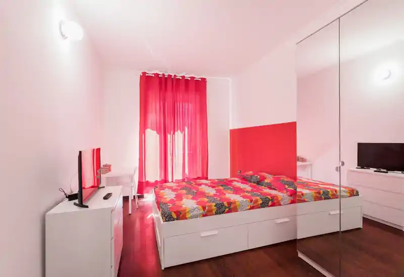 Bright, modern bedroom with a large white platform bed, colorful bedding and mirrored wardrobe creating a sense of space.