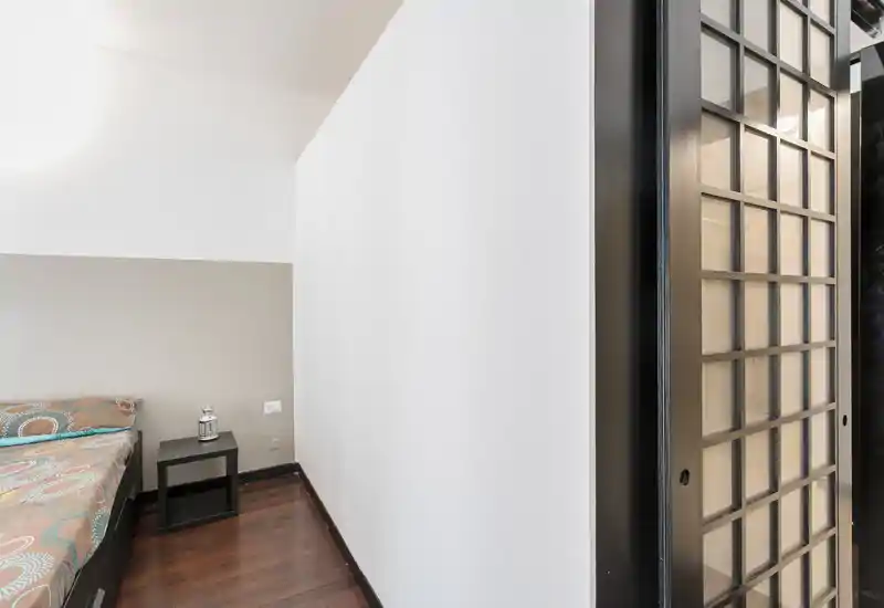 Rincón de dormitorio minimalista con cama estampada, mesita de noche y luz natural suave; líneas limpias y suelo de madera cálido.