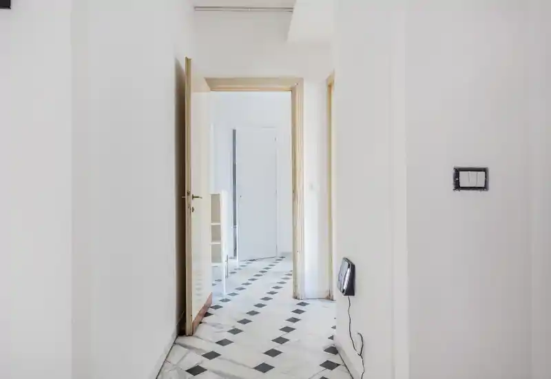 Ingresso luminoso e minimale con pavimento in marmo a motivo e pareti bianche; porte conducono alle stanze adiacenti e la luce naturale illumina l'ambiente.