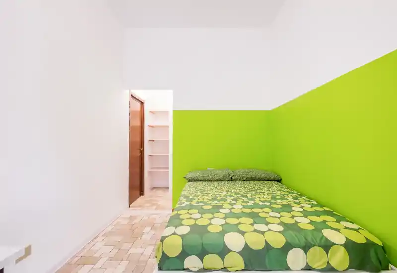Dormitorio luminoso con una cama completa vestida con ropa de cama verde de estampado circular frente a una pared accentuada en verde lima; ambiente limpio, moderno y bien iluminado, ideal para una estancia acogedora.